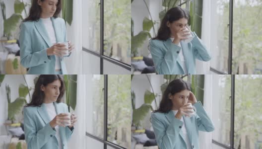 年轻的女商人享受着她的早晨咖啡或茶，看着窗外。漂亮的拉丁女人在办公室里喝着热饮。高清在线视频素材下载