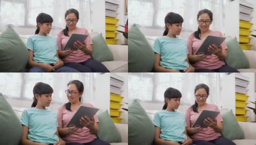快乐的亚洲母亲和她十几岁的女儿坐在家里客厅的沙发上使用数码平板电脑高清在线视频素材下载