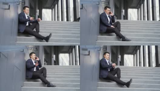 年轻的亚洲人沮丧地坐在楼梯上的街道附近的办公商业中心大楼高清在线视频素材下载