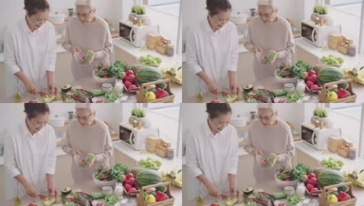 亚洲资深妈妈一边和中间的女儿在厨房准备健康的早餐，蔬菜和水果，一边选择她可以吃的蔬菜，一起享受周末的活动，高角度的正面视图高清在线视频素材下载