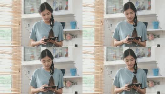 年轻美丽的亚洲女人站在厨房里使用平板电脑和耳机，人们和科技，Z一代的生活方式高清在线视频素材下载