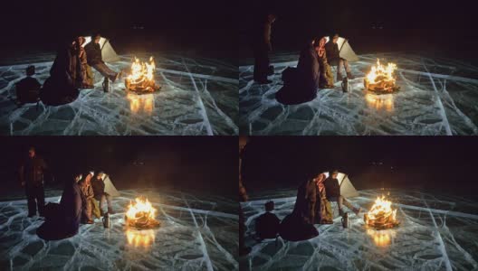 四个旅行者在夜间的冰面上着火。营地在冰上。帐篷紧挨着火。人们围着营火取暖。摄影师在用三脚架拍摄相机。高清在线视频素材下载