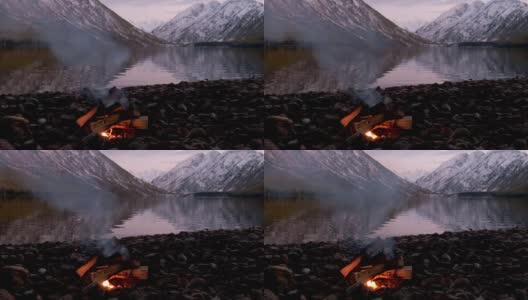 阿尔泰山脉下多恩斯科湖岸边的篝火在深夜，山上覆盖着雪高清在线视频素材下载