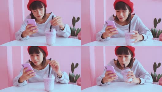 Young asian millennial woman drinking iced bubble milk tea and using smartphone in pink pastel cafe高清在线视频素材下载
