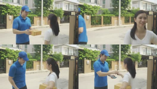 亚洲快递年轻男子在蓝色制服微笑，抱着一堆纸箱在前面的房子和亚洲妇女接受从快递员送的盒子。广告，商业，交通概念。高清在线视频素材下载