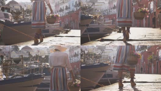 年轻女子提着花篮走在意大利庞扎岛港口的海滨。时尚色彩艳丽的礼服、裙子和帽子。高清在线视频素材下载