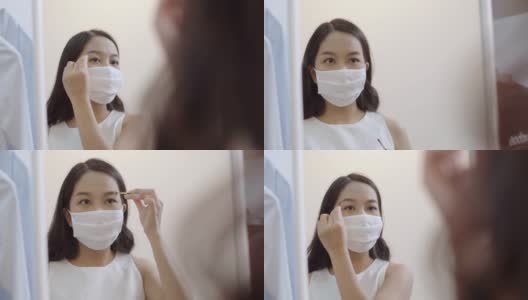 年轻的亚洲妇女戴着防护口罩，在隔离期间画眉毛。高清在线视频素材下载