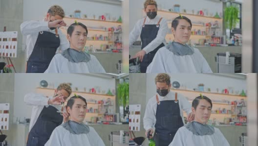 亚洲专业男性发型师在美发厅为年轻顾客梳理和使用剪刀理发。大流行期间，发型师佩戴防护口罩，防止冠状病毒感染。高清在线视频素材下载