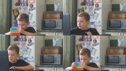 一个7-9岁的白人男孩在家里用笔记本电脑学习，在学习间隙用一个流行的玩具来缓解压力。在家给孩子们玩。这个男孩正在远程学习。本空间高清在线视频素材下载