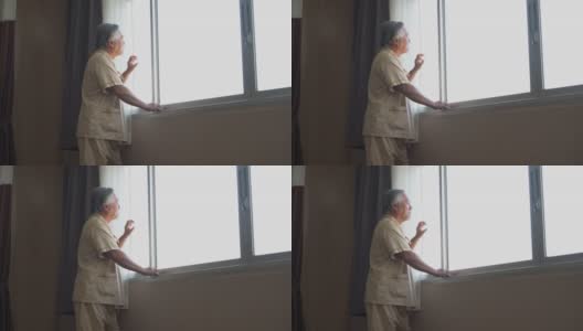 亚洲老年病人站在病房的窗户外。在疗养院里的孤独老人高清在线视频素材下载