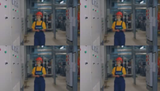 一位年轻的女工程师戴着防护头盔，手里拿着平板电脑，微笑着走向相机。现代工业和生产高清在线视频素材下载