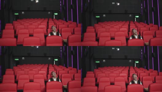 一位留着白胡子的亚裔中国男子坐在空荡荡的电影院的红色座位上一边吃一边看电影。高清在线视频素材下载