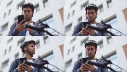 特写脸严肃的年轻人戴着防护头盔，用手机坐在自行车上，从下面拍摄。高清在线视频素材下载