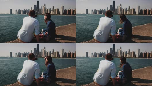 在美国芝加哥的密歇根湖上野餐的年轻夫妇的后视图。男人用智能手机拍照高清在线视频素材下载