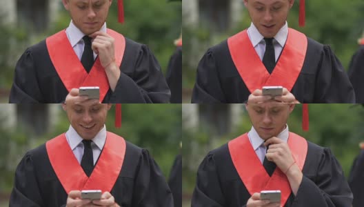 认真的男毕业生一边揉下巴一边看手机，收到了好消息高清在线视频素材下载