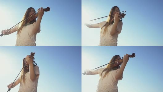 年轻美丽的白人女孩穿着牛仔裤拉着小提琴停留在蓝色的大海背景，慢镜头高清在线视频素材下载