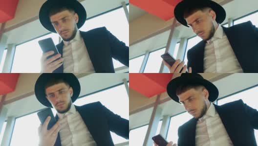 一名穿着黑色西装、戴着帽子的时髦白人男子手持手机，在机场看信息，特写，慢镜头高清在线视频素材下载