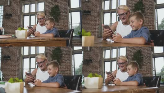 一位戴眼镜的中年白人妇女和她的孙子一起坐在舒适的办公室里的桌子旁，一边在平板电脑屏幕上演示一边说着什么高清在线视频素材下载