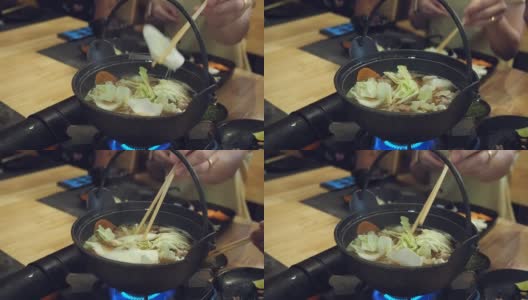 在一家日本餐馆里，一位妇女用筷子把花椰菜放进了涮锅里。高清在线视频素材下载