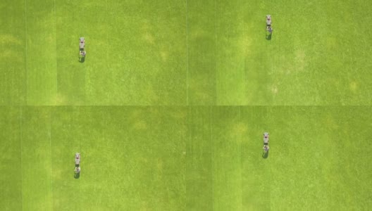 鸟瞰图:夏季足球场上用割草机修剪青草的工人的小身影。高清在线视频素材下载