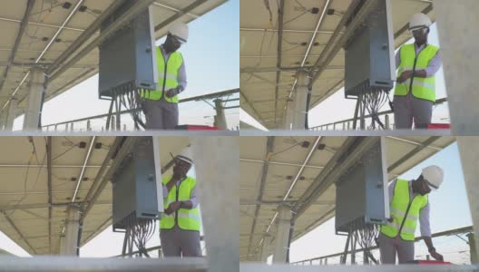 在太阳能发电厂的控制面板上，身穿有反光布的防护服的非洲年轻工程师通过无线电与他的团队联系，帮助他们检查和修复电力系统高清在线视频素材下载