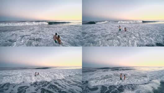 日落时分，一名年轻男子和一名少女在海里游泳，被海浪击中。汉普顿海滩，长岛，纽约州，美国。高清在线视频素材下载