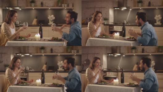 一对美丽的夫妇在厨房里吃烛光晚餐。他们喝酒、吃饭、聊天。两个都有好心情和微笑很多。高清在线视频素材下载