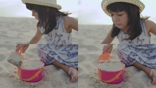 一个小女孩在沙滩上用铲子和水桶玩沙子高清在线视频素材下载