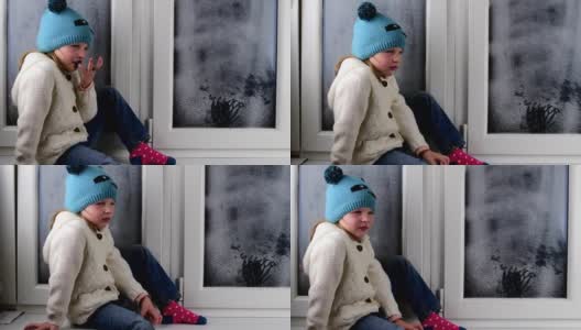 小女孩坐在结冰的窗户后面的窗台上。低的自由度。高清在线视频素材下载