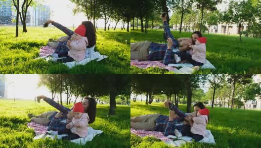 幸福的家庭躺在格子布上，在日落时分和一个婴儿在公园里自拍。爸爸妈妈和宝宝合影高清在线视频素材下载