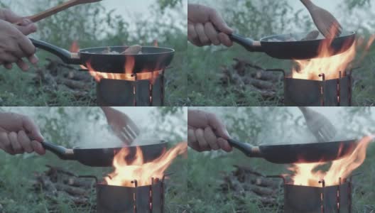 森林里野餐时，一名男子在篝火上用煎锅煎肉。高清在线视频素材下载