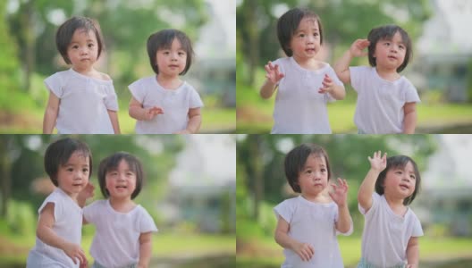 在草坪公园里，一对可爱的亚洲华人双胞胎男婴向他们的父母挥手高清在线视频素材下载