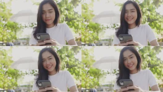 美丽的亚洲少女在社交媒体上用智能手机开心地微笑在夏季花园。在手机触摸屏上给家人写祝福信息。社会网上购物。在家网上订购高清在线视频素材下载