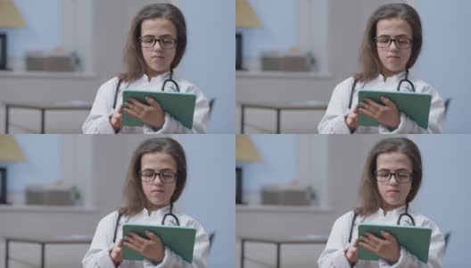 自信聪明的女医生的肖像，戴着眼镜，大拇指向上，微笑地看着相机，站在室内平板电脑。快乐的白人小人在医院摆姿势工作。高清在线视频素材下载