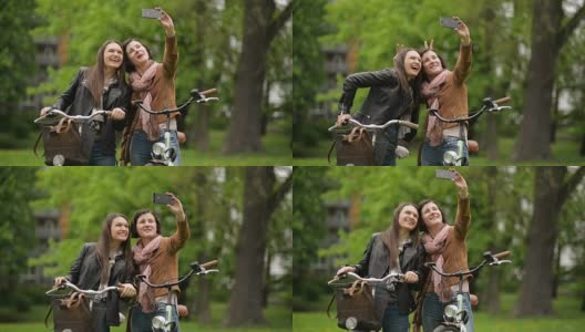 有趣的女性朋友拿着自行车用智能手机自拍。春天的城市公园里，两个女孩正在用手机自拍高清在线视频素材下载