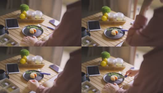 亚洲华人女子在客厅切雪皮月饼，享用中国传统节日甜点的下午茶高清在线视频素材下载