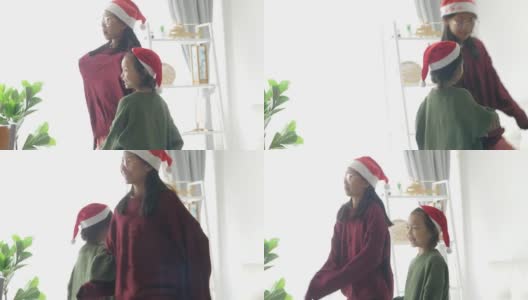 快乐的亚洲儿童戴着圣诞帽和毛衣一起在家里的窗户附近跳舞，圣诞概念。高清在线视频素材下载