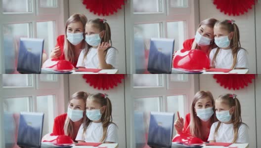 妈妈和女儿戴着医用口罩，通过笔记本电脑通过视频交流来祝贺情人节。2月14日是一个远离新冠肺炎疫情的节日。高清在线视频素材下载