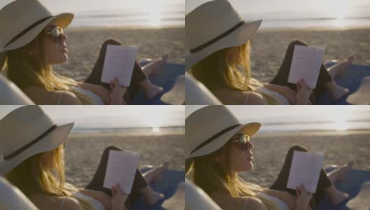 年轻迷人的女人坐在美丽的海滩上看书高清在线视频素材下载
