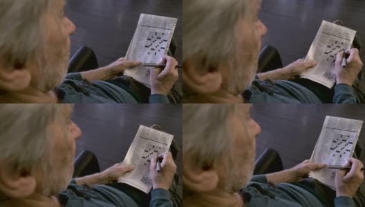一位老人坐在椅子上玩着OTS报纸上的填字游戏高清在线视频素材下载