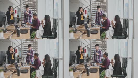 亚洲同事和坐在轮椅上的印度同事在办公室的工作站上分享面包点心高清在线视频素材下载