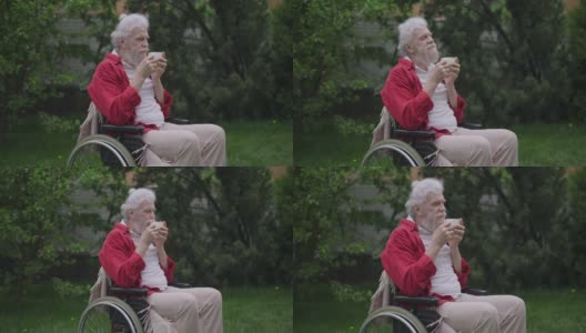 在春天的户外花园，残疾人一边闻一边品尝美味的卡布奇诺。白发残障的白人退休老人的肖像在慢动作享受热饮。高清在线视频素材下载
