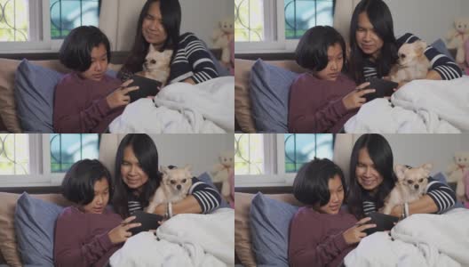母女二人用平板电脑视频通话，在卧室里和狗狗玩耍。幸福的家庭的概念。高清在线视频素材下载