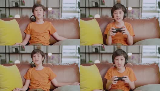 亚洲男孩流媒体游戏在线沉迷于智能手机游戏手机戴耳机，退出了亚洲男孩手玩智能手机游戏在线通过互联网在家里的沙发上，呆在家里的想法概念高清在线视频素材下载