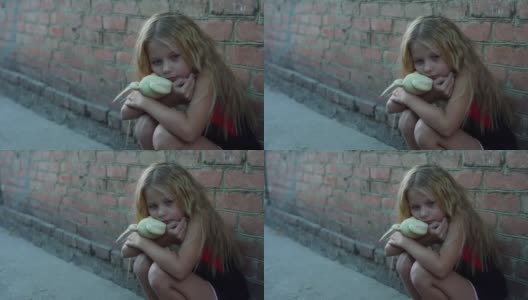 一个孤独，害怕的女孩的肖像，美丽的凌乱的头发坐着，她的玩具靠着砖墙。高清在线视频素材下载