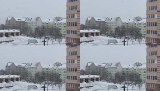 下雪了。模糊的背景，在住宅建筑的背景下飘落的大片雪花。丰富的雪花。从公寓看到的景色高清在线视频素材下载