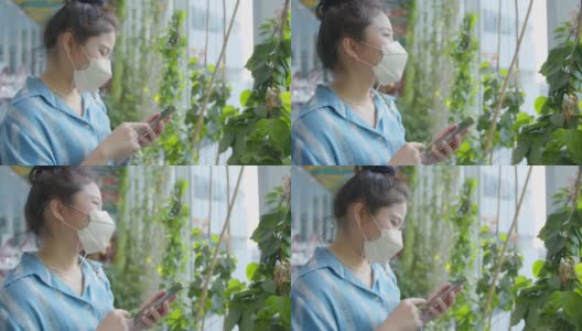 迷人的亚洲女性休闲服戴口罩防毒手用智能手机数码设备在花园树在商场超市背景高清在线视频素材下载