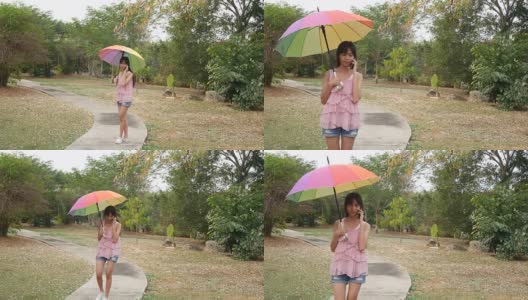 亚洲十几岁的女孩走在花园里用花哨的雨伞和使用电话高清在线视频素材下载