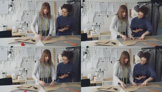 一位女服装设计师正在用粉笔在布料上画出新衣服的轮廓，而她的同事正在用写字板帮助她。技术在服装制造的概念。高清在线视频素材下载
