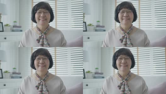 肖像快乐的资深亚洲妇女放松地坐在家里的公寓沙发沙发看相机享受退休或检疫时间微笑。有吸引力的亚洲成年人老年人幸福的生活方式。高清在线视频素材下载